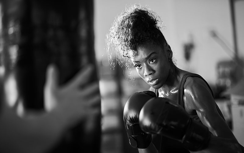 african woman boxing with punching bag in garage gym
