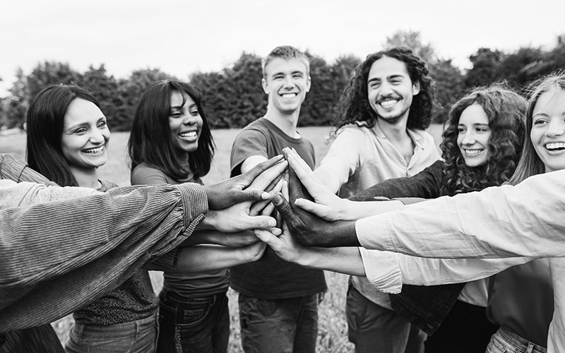 Young diverse team having fun stacking hands outdoor - Focus on hands - Black and white editing
